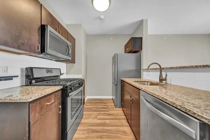 Modern kitchen with sleek stainless steel appliances, energy efficient appliances, rich wood cabinetry, and elegant granite countertops in a studio apartment.