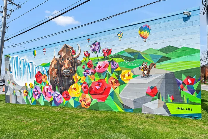 Vibrant mural featuring a geometric buffalo amidst colorful polygonal roses, the NYS flower, and hot air balloons against Niagara Falls backdrop.