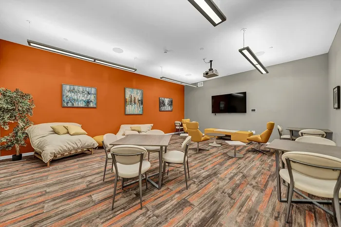 Lounge area and media room with vibrant orange accent wall, modern seating, large flat-screen TV, and abstract artwork, perfect for relaxation, movie nights, and social gatherings.