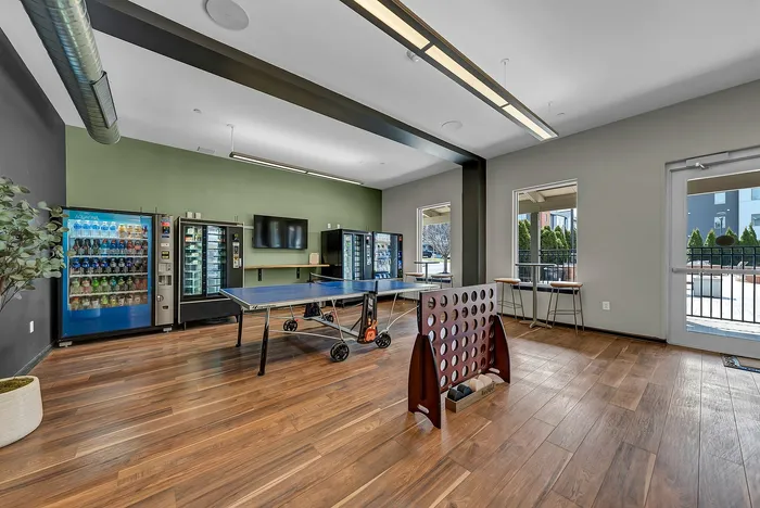 Modern recreation room featuring a ping pong table, vending machines, and a large Connect Four game, with natural light streaming in through windows.