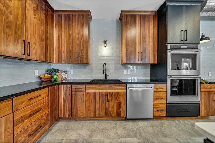 Luxury apartment communal kitchen with rich wooden cabinetry, modern stainless steel appliances, and sleek black countertops, ideal for culinary enthusiasts.