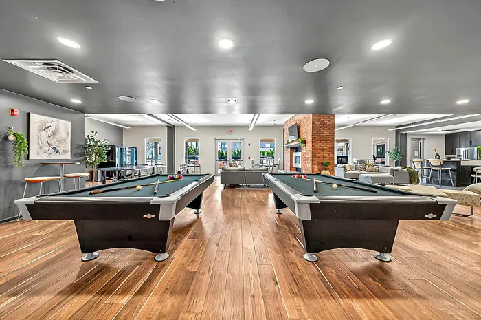 Luxury apartment community entertainment space featuring sleek pool tables, modern seating, and a cozy fireplace, perfect for social gatherings.