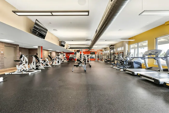 Spacious, modern apartment complex fitness gym with state-of-the-art equipment and vibrant decor, perfect for an energetic workout. Lots of treadmills and other workout equipment.