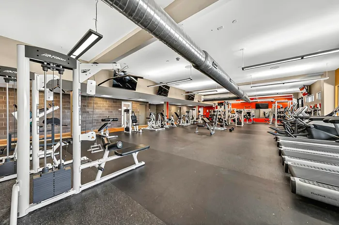 Spacious modern apartment community fitness gym with state-of-the-art fitness equipment, offering a vibrant workout environment with ample natural light.