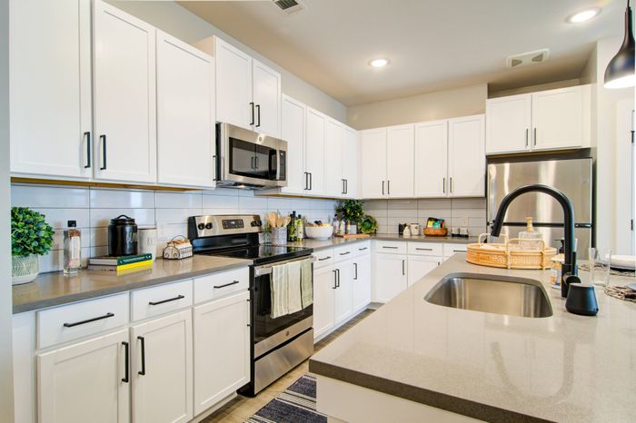 Sugar Hill, GA Apartments - Cadence Sugar Hill - Modern Kitchen with Stainless-Steel Appliances, White Cabinets, Black Fixtures, and Kitchen Island