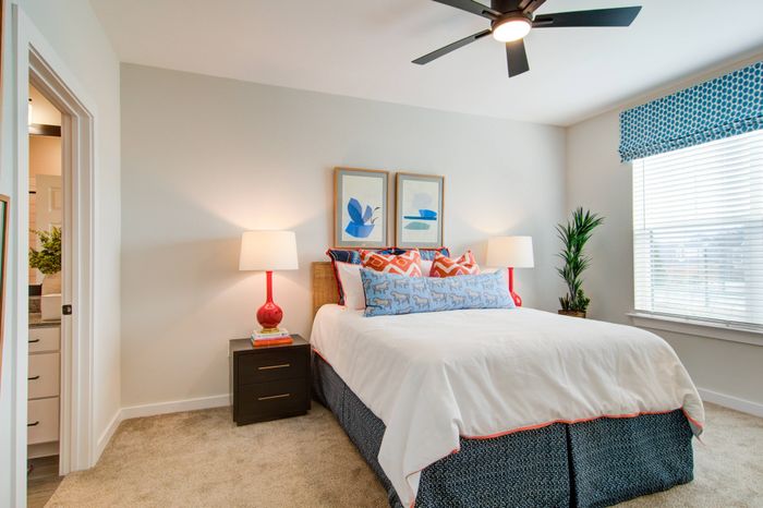Dog-Friendly Apartments In Sugar Hill GA - Bedroom With Bed, Modern Decor, Nightstands, Lamps, Ceiling Fan, Window, And Attached Bathroom.