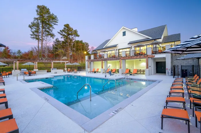 Two-BR Apartments In Sugar Hill GA - Pool With Lounge Chairs, Umbrellas, Clubhouse, And Trees In The Background.