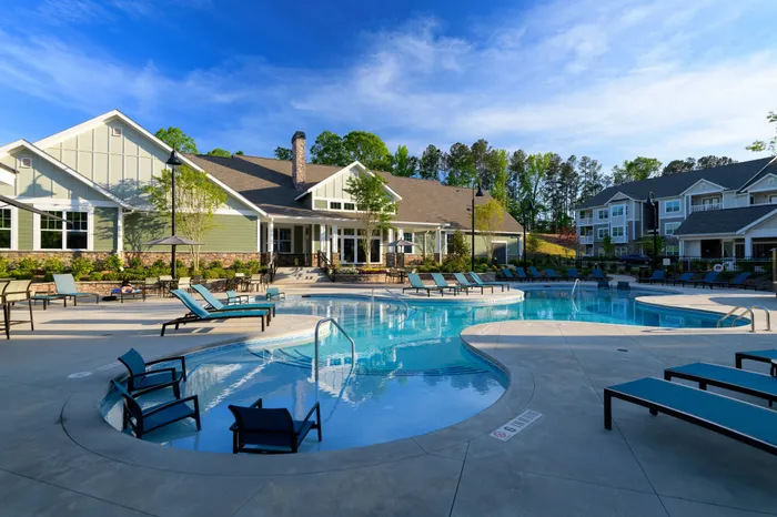 Athens, GA Apartments - Lullwater at Jennings Mill - Pool With Lounge Chairs, In-Pool Seating, and Beautiful Landscaping In Front of the Community Building