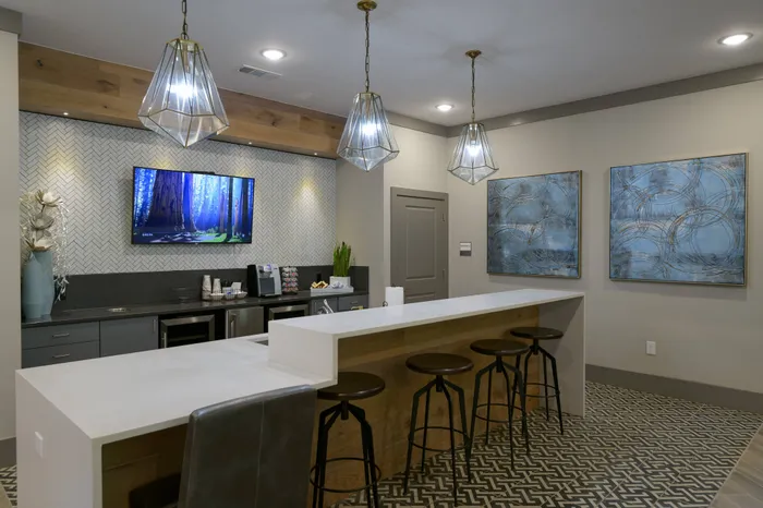 Athens Apartments - Lullwater at Jennings Mill - Resident Clubhouse Kitchen with Long White Counter, Stool Seating, TV, Coffee Station, and Hanging Overhead Lighting