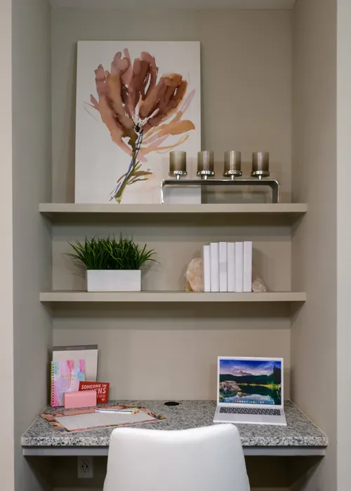 Two-Bedroom Apartments in Athens, GA - Lullwater at Jennings Mill - Built-In Computer Nooks With Granite Work Surface, Open Shelving, Laptop Setup, Decorative Wall Art, And White Desk Chair.