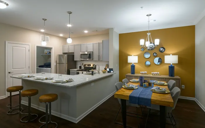 2-Bedroom Apartments in Athens, GA - Lullwater at Jennings Mill - Modern Kitchen And Dining Area With Granite Breakfast Bar, Stainless Steel Appliances, Pendant Lighting, And Accent Wall.