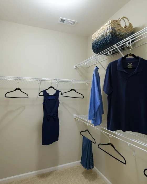 Apartments in Athens for Rent - Lullwater at Jennings Mill - Spacious Closet with White Metal Shelving at Different Levels, with Some Clothing Hanging on Black Hangers