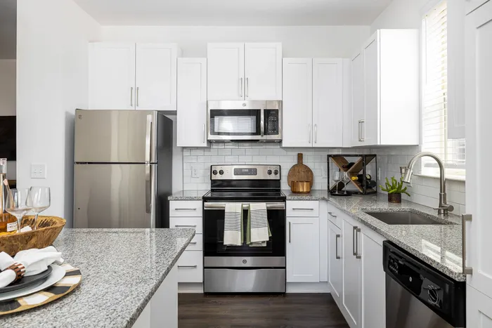 Buford, GA, Apartments - The Harrison at Braselton - Kitchen with White & Shaker Cabinetry, a Kitchen Island, Granite Countertops, Stainless Steel Appliances, and White Subway Tile Backsplash