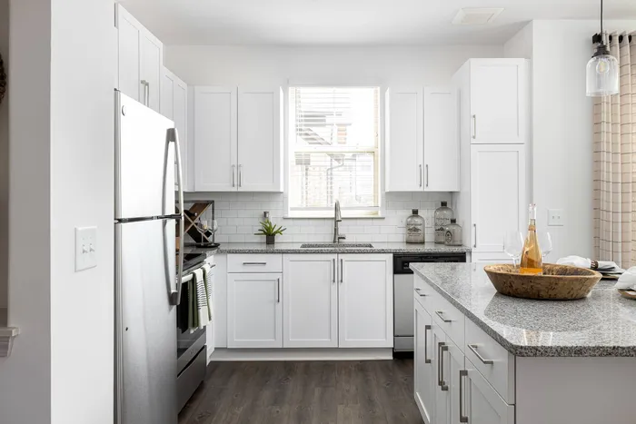 Dog-Friendly Apartments in Buford, GA - The Harrison at Braselton - Kitchen with Island, Wood-Style Plank Flooring, White Shaker Cabinetry, Subway Tile Backsplash, and Stainless-Inspired Appliances.