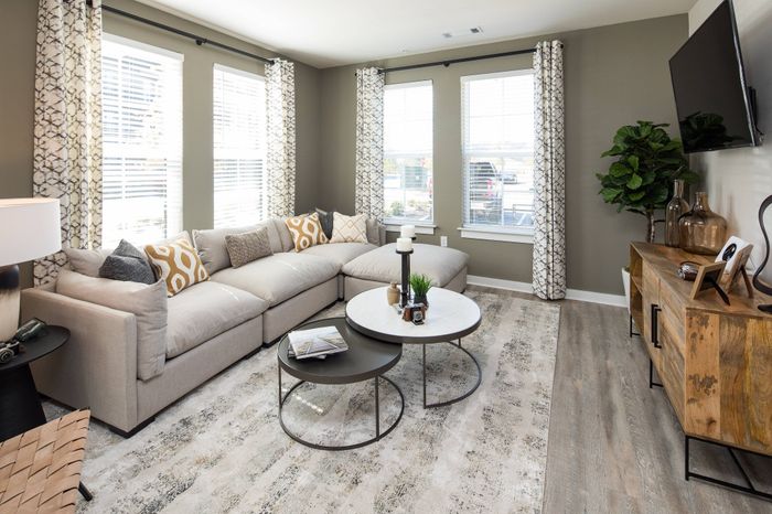 Gainesville, GA Apartments - The Mill at New Holland - Living Room with Spacious Windows, Large Sectional Couch, Tall Wooden Media Consule, and Wood-Style Flooring