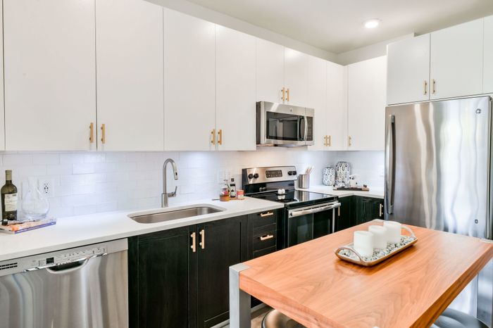 Forest Park, AL Apartments - Park 35 on Clairmont - Modern Kitchen with White Cabinetry, Stainless Steel Appliances, Tile Backsplash, Quartz Countertops, Cooking Island with Wood Surface, Metal Legs, and Stool Seating