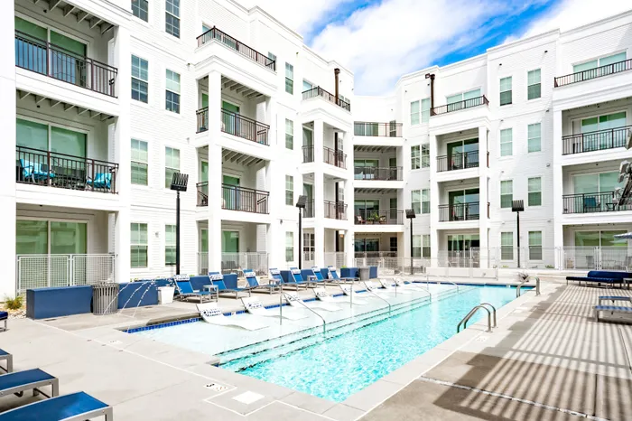 Pet-Friendly Apartments in Downtown Birmingham AL - Park 35 on Clairmont - Pool Area with Submerged and Poolside Lounge Chairs, Fountain Spray, and View of Surrounding Building Exterior