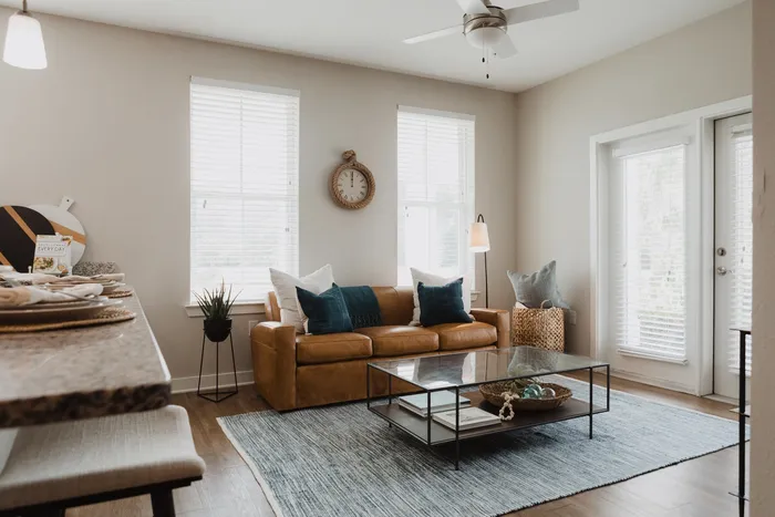 Furnished living room with leather couch, ceiling fan and windows