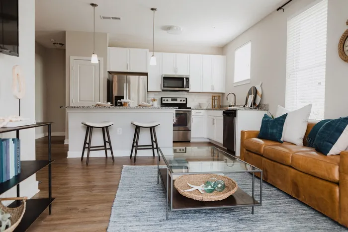 View of the kitchen with stainless steel and black appliances with living room with leather couch in view