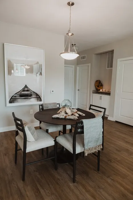 Furnished dining room with round dining table and four dining chairs with art on the wall and light hanging over table