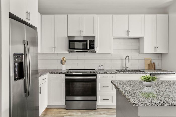 1-Bedroom Apartments in Matthews, NC - Chestnut Farm - Modern Kitchen with Stainless Steel Appliances, White Cabinets, White Tile Backsplash, Granite Countertops, Wood-Inspired Plank Flooring, and a Kitchen Island