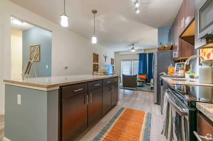 Modern kitchen with sleek countertops opening into a cozy living room featuring stylish decor and natural lighting.