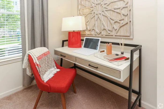 Inviting home office setup with a red chair, modern desk, and bright table lamp.