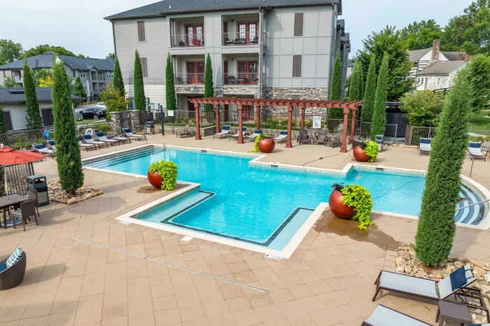 Inviting apartment complex with a modern pool, stylish pergola, lounge chairs, and lush greenery.