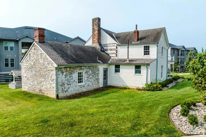 Exterior view of a charming historic stone and wood house with a lush green lawn, surrounded by modern apartments.