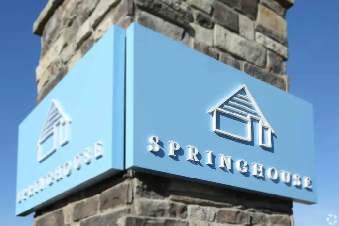 Elegant blue sign with a house icon and the word 'SPRINGHOUSE' displayed on a stone column.