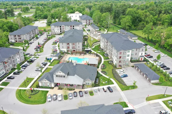 Aerial view of a modern apartment complex featuring multiple residential buildings, a central swimming pool, and landscaped pathways.