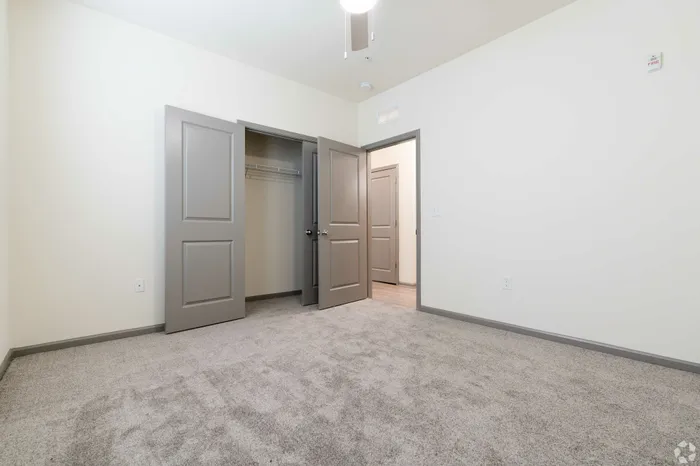 Bright and airy bedroom with plush carpeting, open closet doors, and subtle modern design.