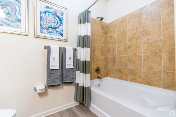 Chic bathroom featuring a stylish bathtub with beige tile surround, colorful abstract art, and plush towels.