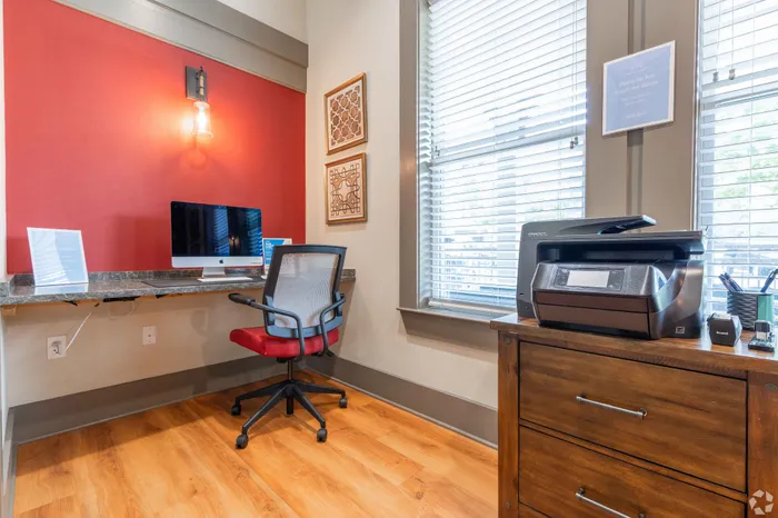 Bright and efficient office nook featuring a desk with a modern computer setup, a comfortable chair, and a multifunction printer.