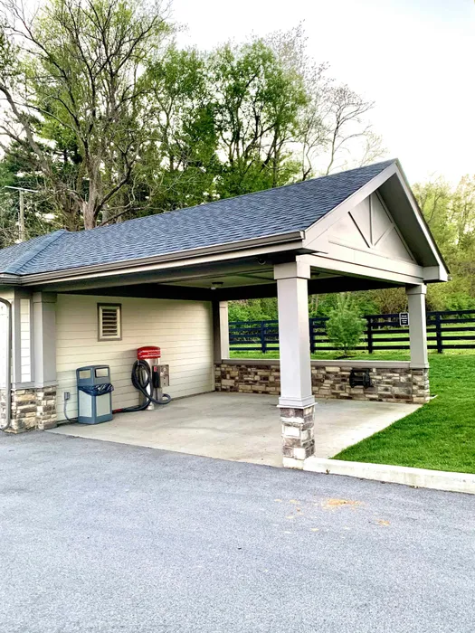 Charming covered carport surrounded by lush greenery, featuring stone accents and a convenient vacuum station.