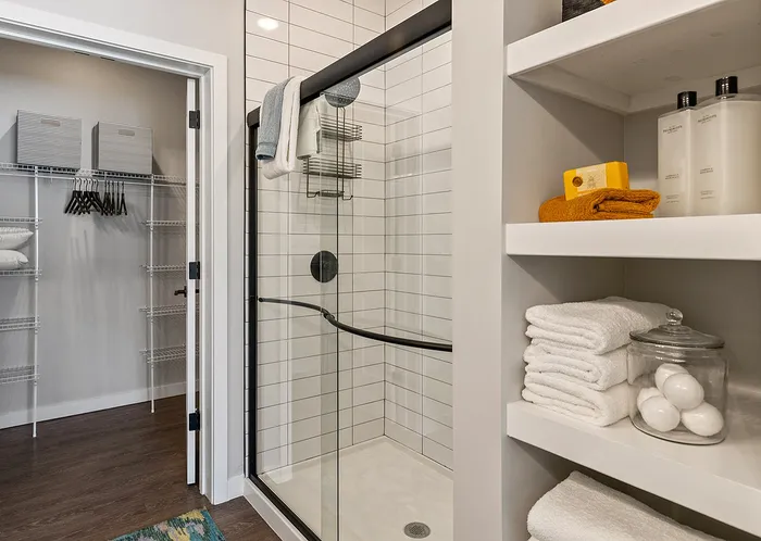 Modern bathroom featuring a sleek glass shower, neatly organized closet, and elegant shelving stocked with plush towels and toiletries.