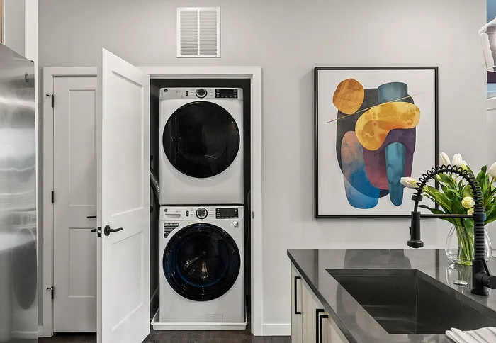 Modern kitchen corner with sleek stainless steel appliances, stackable washer and dryer, vibrant abstract art, and elegant faucet with flowers.