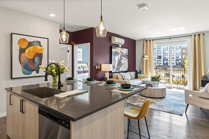 Bright open-concept living room with modern kitchen island, elegant decor, and large sliding glass doors leading to a sunlit balcony.