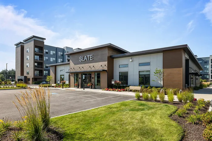 Modern apartment complex exterior with sleek architecture and beautifully landscaped surroundings under a clear blue sky.