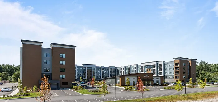 Contemporary apartment complex with lush landscaping and ample parking, set under a bright blue sky.