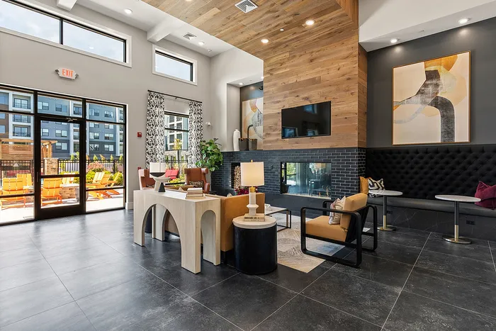 Modern apartment lobby with stylish decor, high ceilings, cozy seating, and a stunning wood-paneled fireplace.