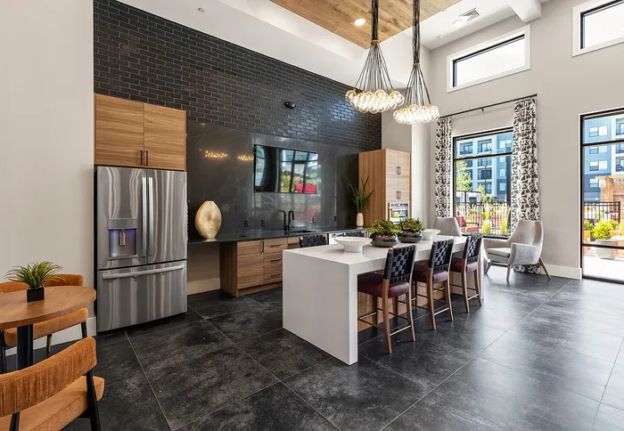 Modern kitchen with sleek black tile wall, elegant pendant lighting, and large windows overlooking a vibrant exterior.