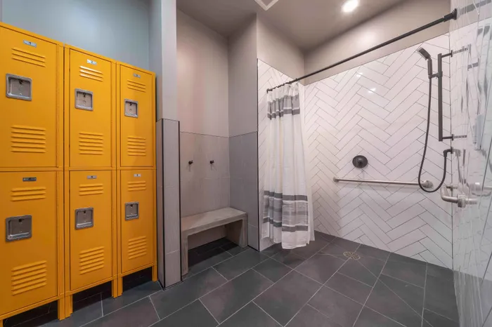 Modern locker room with vibrant yellow lockers, sleek shower area with stylish white herringbone tiles, and convenient bench seating.