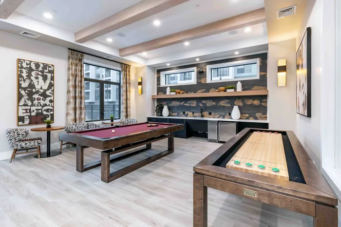 Luxurious game room with a modern pool table and shuffleboard, featuring stylish decor and ample natural light.