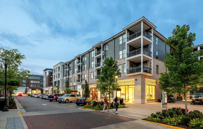 Charming urban apartment complex with modern architecture, vibrant storefronts, and cozy balconies set against a picturesque evening sky.