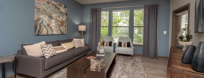 Contemporary living room with sleek gray sofa, elegant art piece, chic decor, and large windows featuring tranquil garden views.