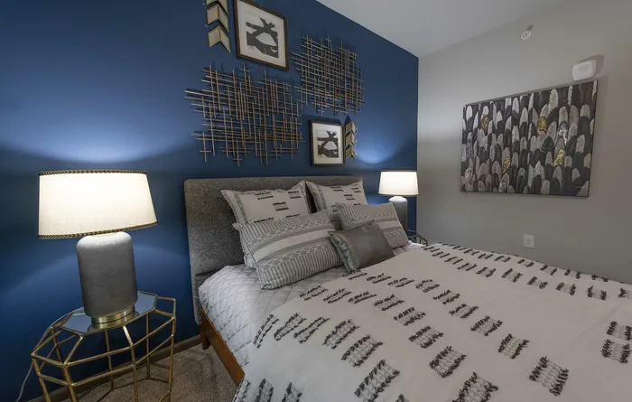 Elegant bedroom with a modern design featuring a plush bed, artistic wall decor on a blue accent wall, and soft ambient lighting.