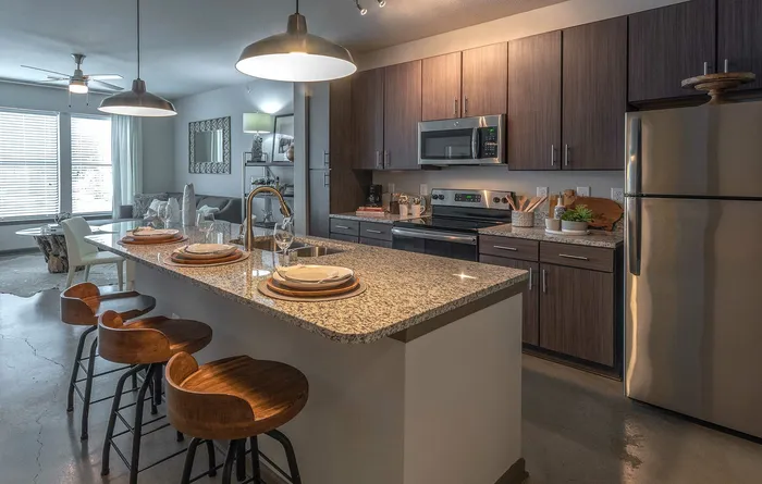 Contemporary kitchen and living area featuring sleek granite countertops, modern appliances, and chic dining space with stylish pendant lighting.