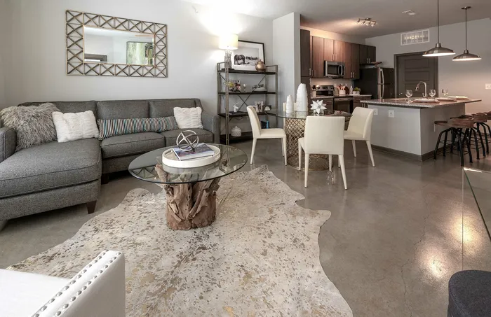 Contemporary living room with plush gray sectional, elegant decor, and open-concept kitchen and dining area featuring sleek furniture and modern lighting.