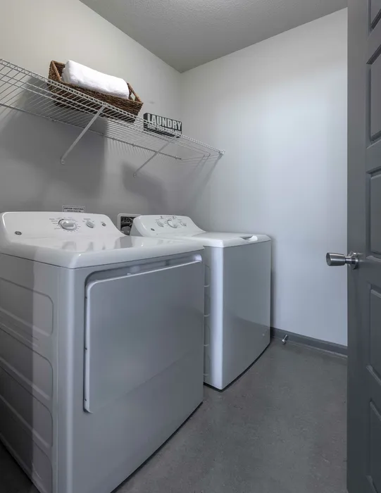 Chic and modern laundry room featuring sleek white washer and dryer with overhead storage shelf.